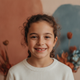 Headshot portrait of a happy young girl smiling, against a soft background with terracotta and slate blue tones.
